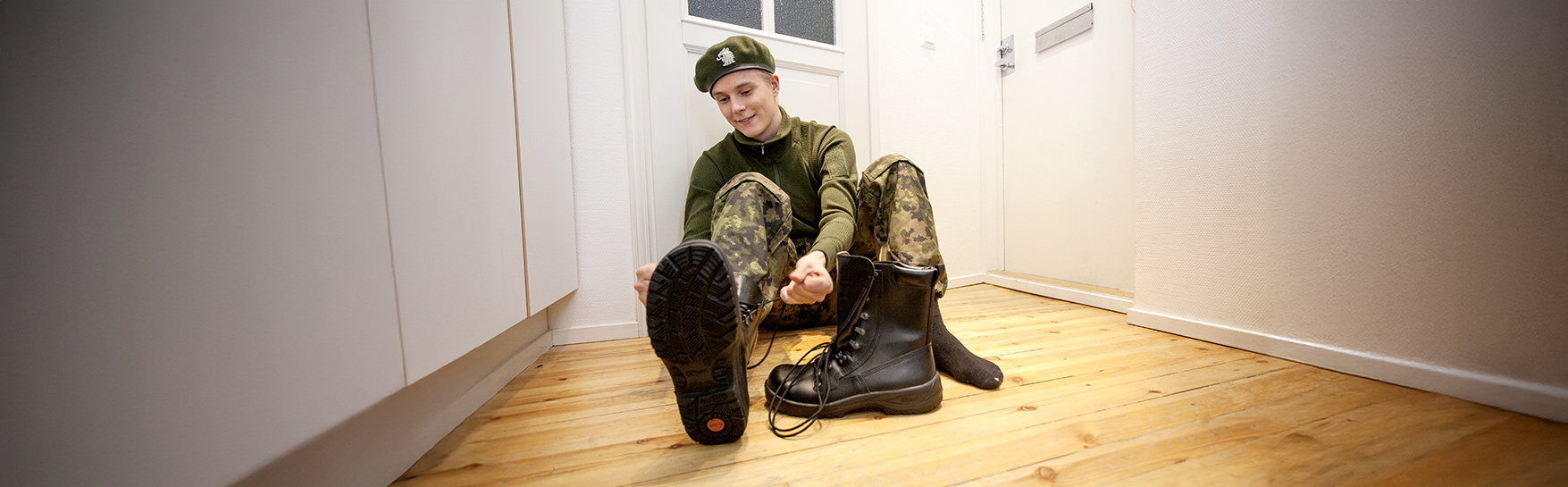 Asepalveluksessa oleva henkilö pukee kenkiä jalkaansa.